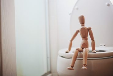 Small wooden artist's model sitting on a real-lift toilet